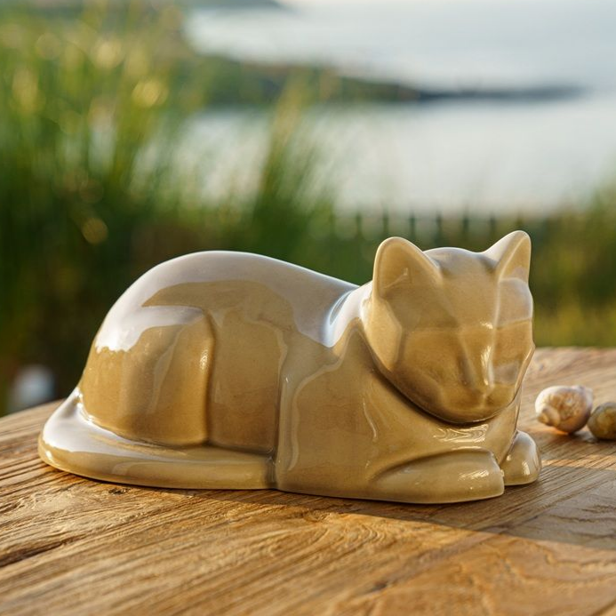 Tan ceramic cat figurine resting on a wooden surface, with a blurred outdoor background.