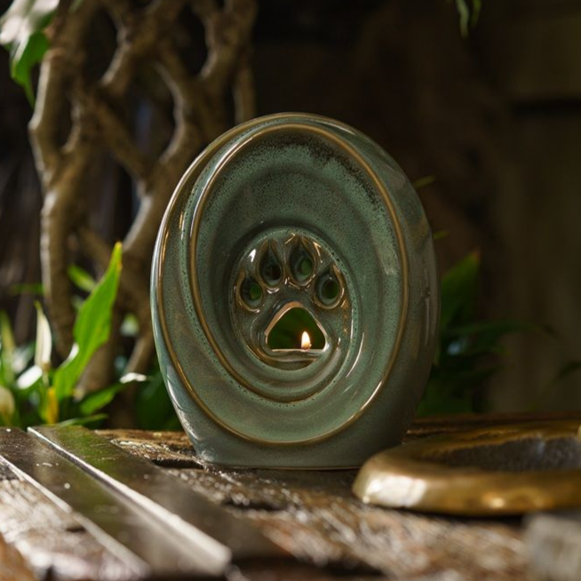 Green ceramic pet urn with paw print cutout and lit candle.