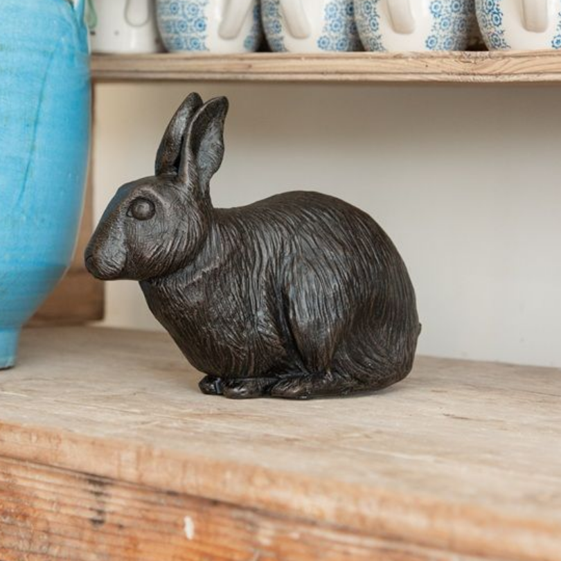 Black rabbit statue on a wooden shelf, next to a blue vase and white mugs.