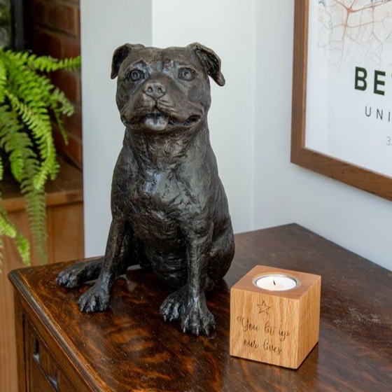 Bronze Staffordshire bull terrier statue on a wooden table with a candle holder.