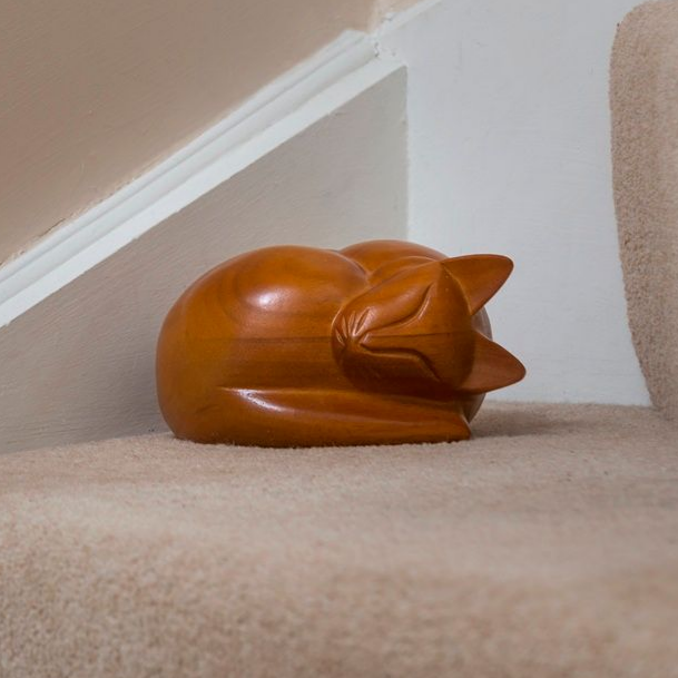 Wooden cat sculpture curled up on a carpeted staircase.