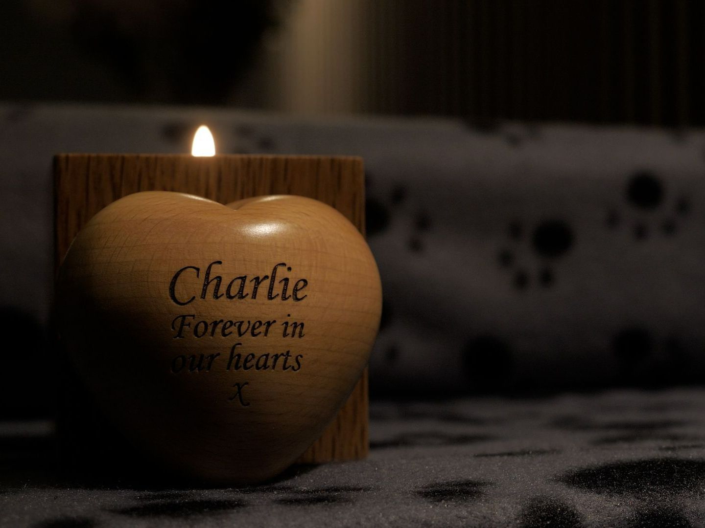 Lit candle in heart-shaped wooden holder engraved