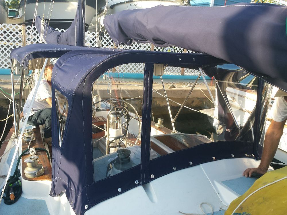 A dark blue canvas sailboat dodger frame installed on a deck, with people working in the cockpit area.