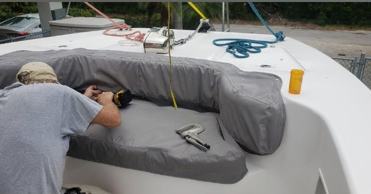 Person working on a boat seat with gray cushions and tools on deck during maintenance.