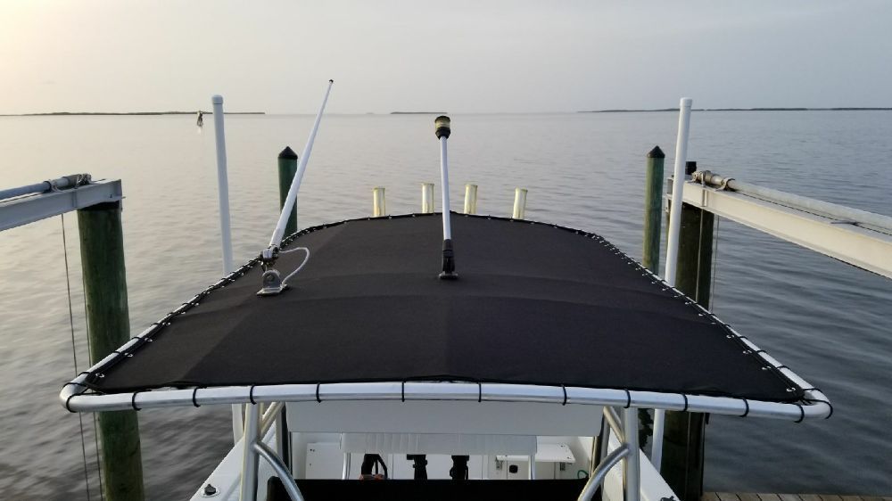 A boat parked at a wooden dock, featuring a black canvas top with a white frame, antenna, and light against a calm water.