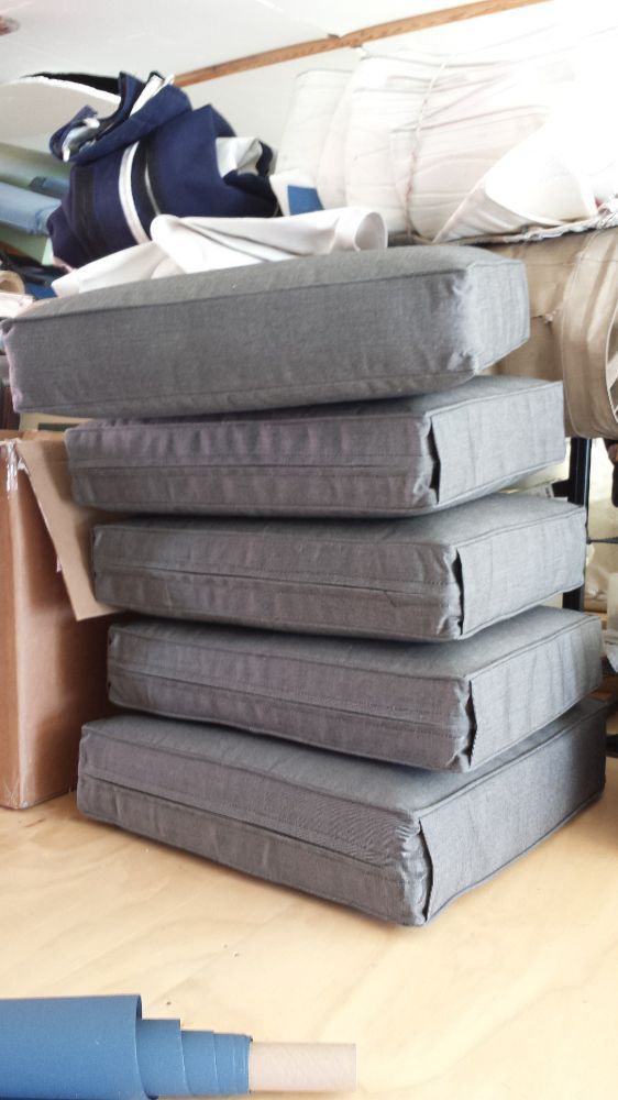 A stack of five rectangular, grey fabric cushions rests on a wooden surface in a storage area.