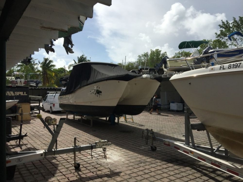 Two boats on trailers parked on a paved lot under a partially covered outdoor storage area.
