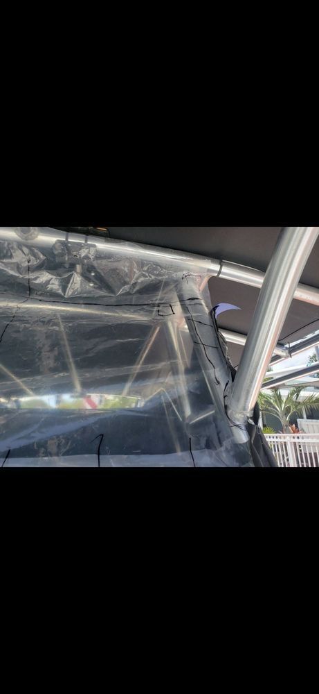 A close-up view of clear plastic boat enclosure panels attached to a metal frame, showing zipper and snaps under a roof.