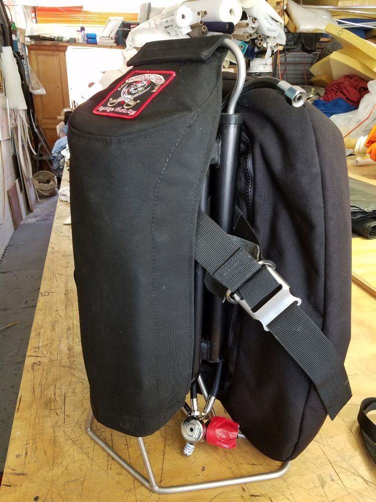 A black fabric scuba diving sidemount harness system with a metal frame and regulator, resting on a wooden workbench.