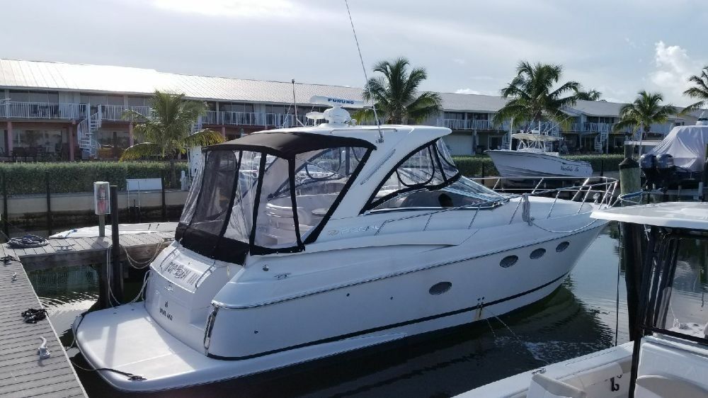A white motor yacht moored at a marina dock with palm trees and buildings in the background.