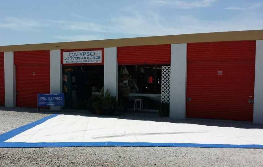 A commercial building with red roll-up doors, white columns, and a storefront entrance featuring a blue-bordered white mat.