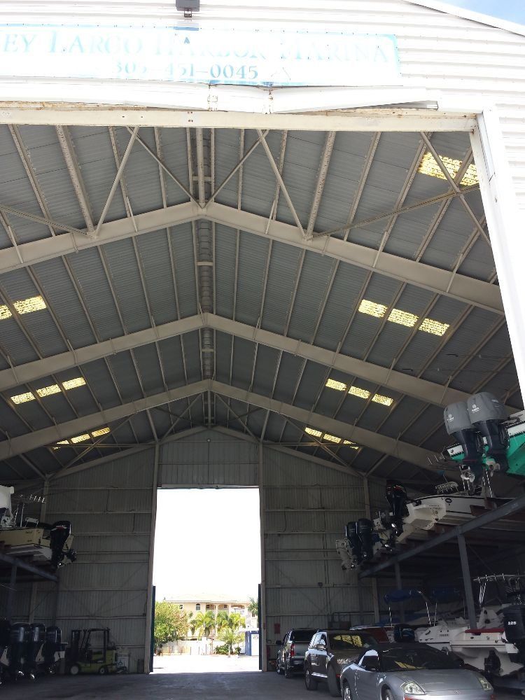 A high-ceilinged, industrial boat storage warehouse containing stacked boats and vehicles, with an open doorway at the back.