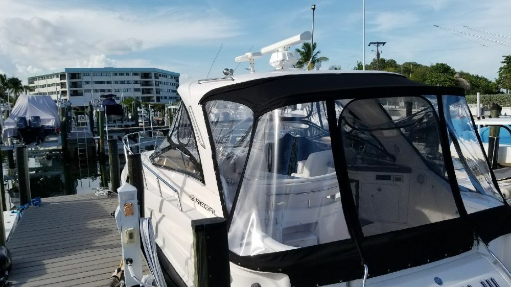 A white motorboat docked at a marina, featuring a clear, protective canvas enclosure over the cockpit area.