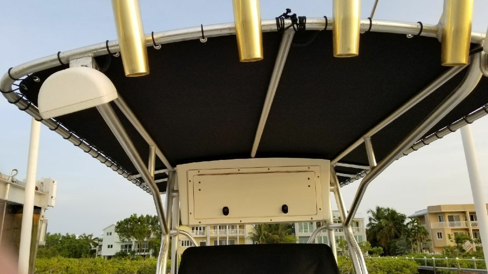 A boat's black T-top canopy with gold rod holders, viewed from below against a background of houses and trees.