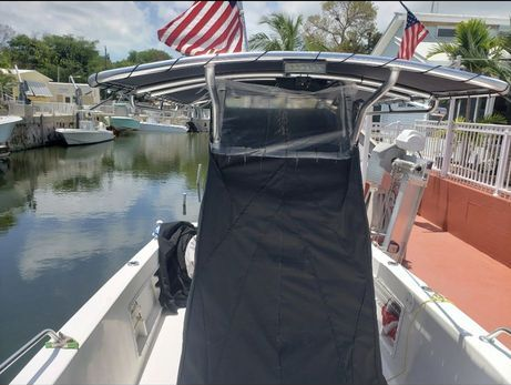 A boat center console covered by a black protective canvas, moored in a canal with an American flag flying on the T-top.