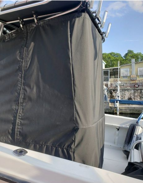 Black canvas boat enclosure cover attached to a metal frame on a boat deck, with a marina in the background.