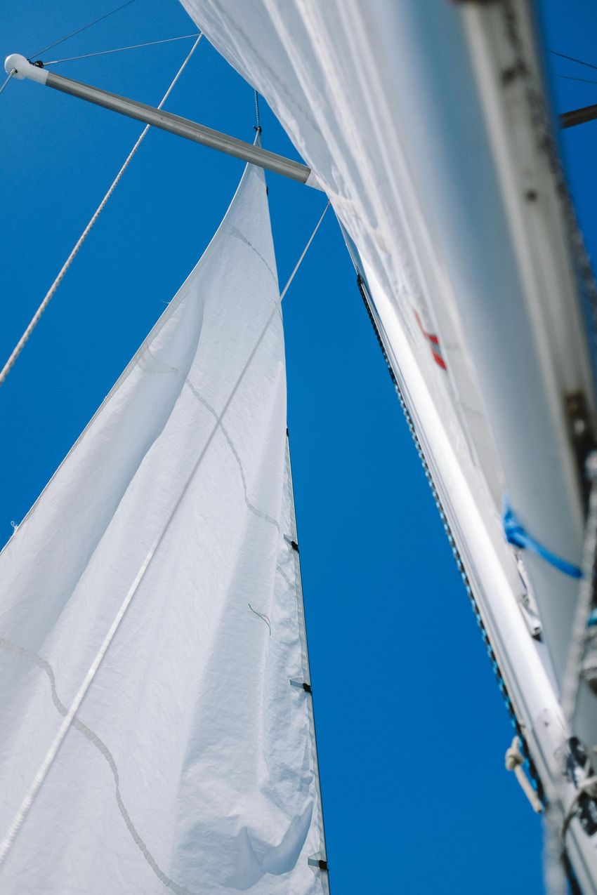 Looking up at the white sails of a sailboat against a clear, bright blue sky.