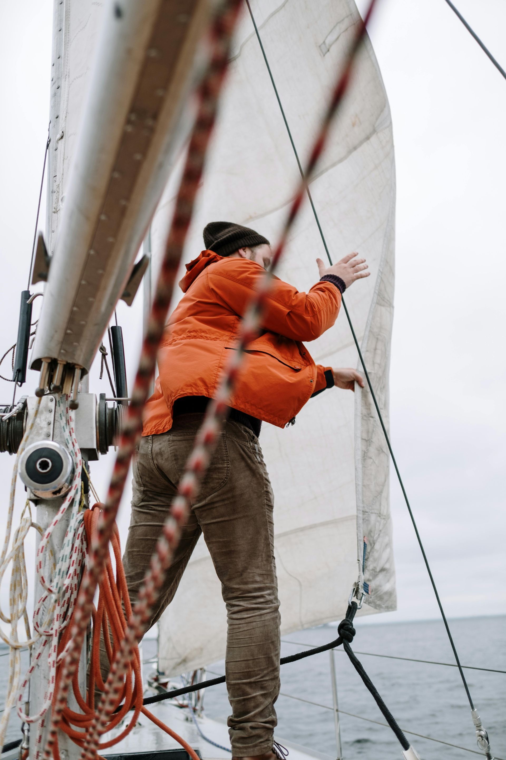 A person in an orange jacket adjusts the sail on a boat on the water.