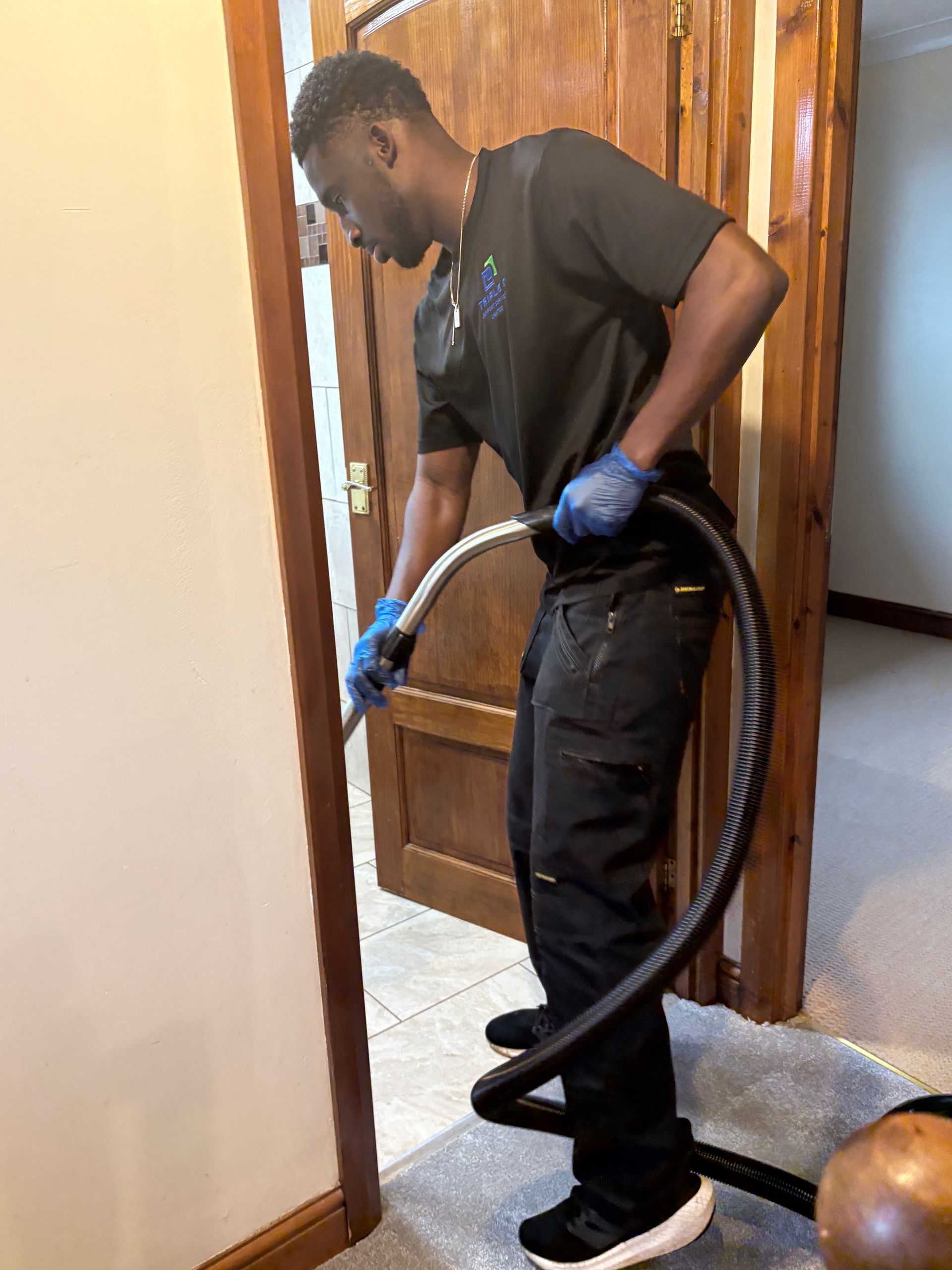 A man in a green shirt and black apron is holding a vacuum cleaner.