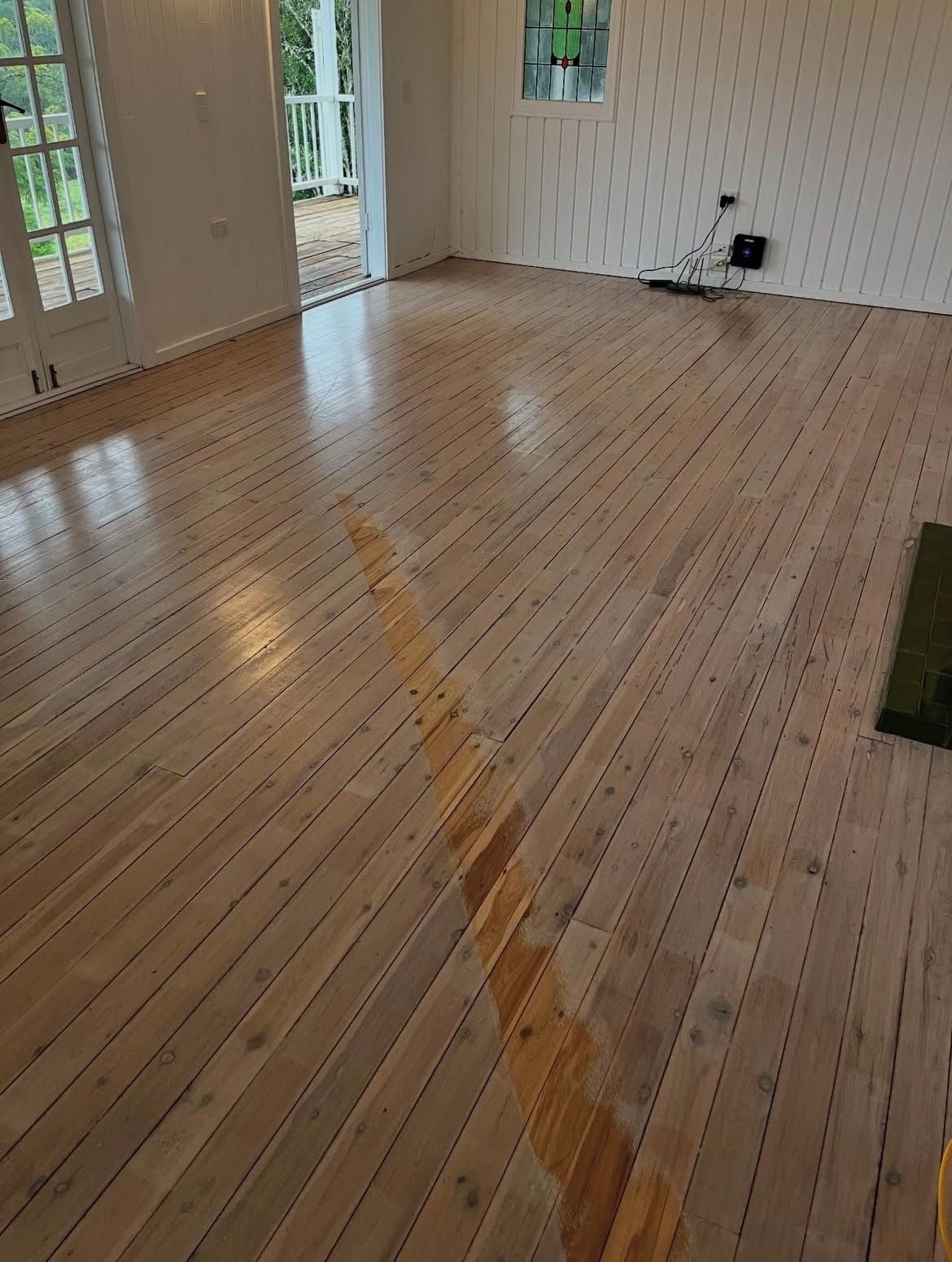 Refinished wooden floor in a room with white walls and a doorway leading outside; light reflects off the shiny surface. — Tweed Coast Cork & Timber Floors In Tweed Heads, NSW