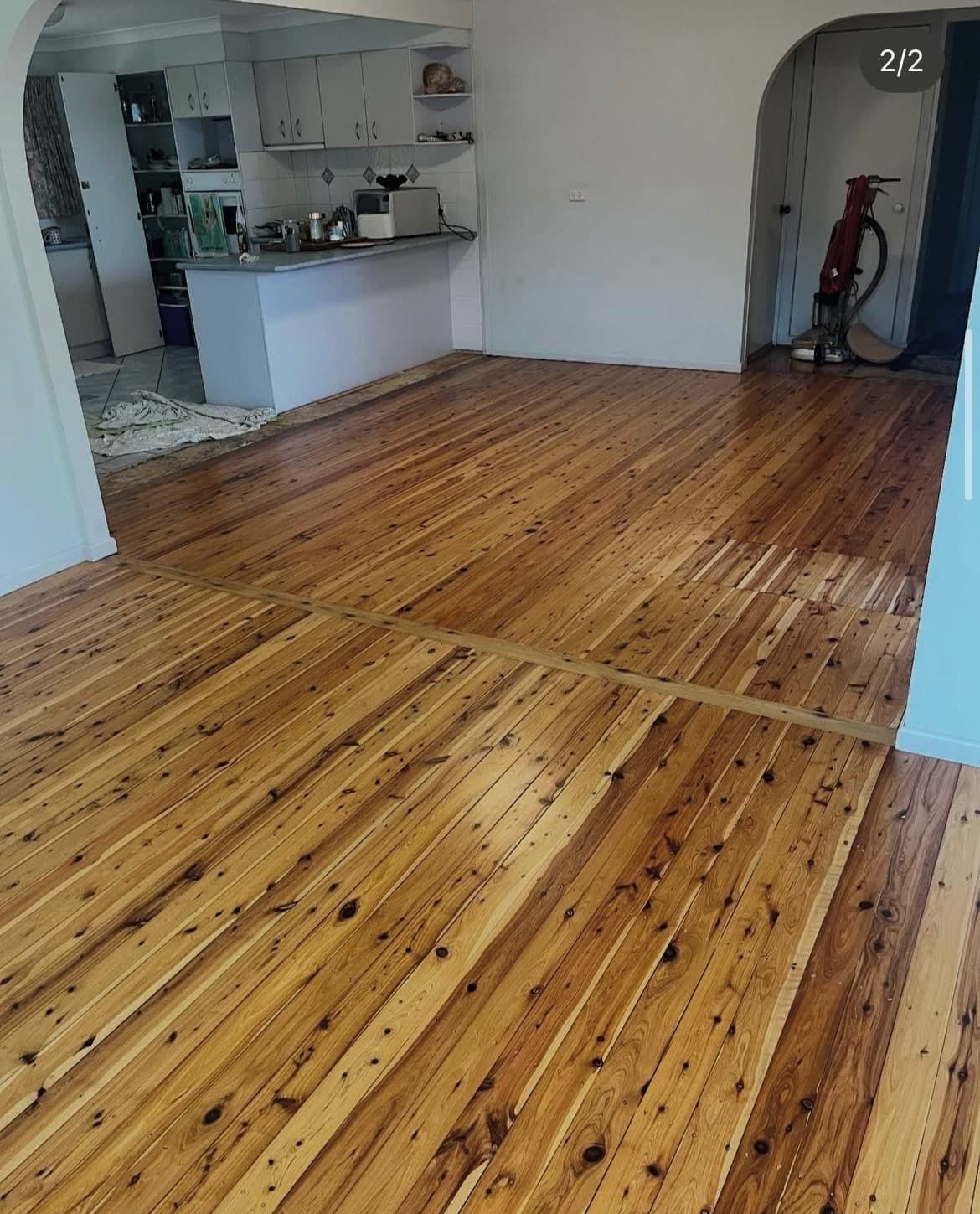 Wooden floor in a room, with a kitchen and doorway visible. Warm, amber tones. — Tweed Coast Cork & Timber Floors In Tweed Heads, NSW