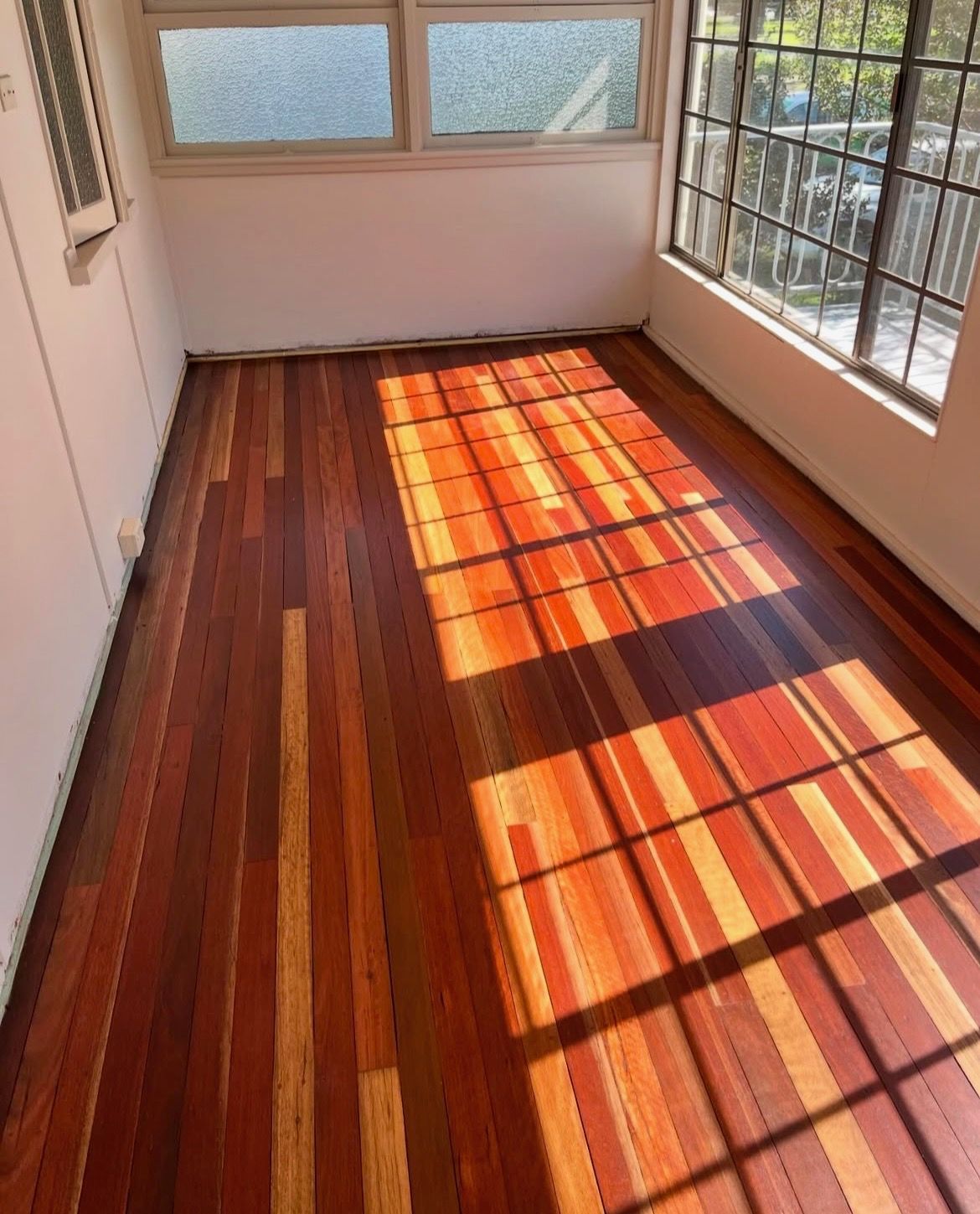 Hardwood floor in a room with sunlight streaming through window. The floor is reddish-brown. — Tweed Coast Cork & Timber Floors In Tweed Heads, NSW