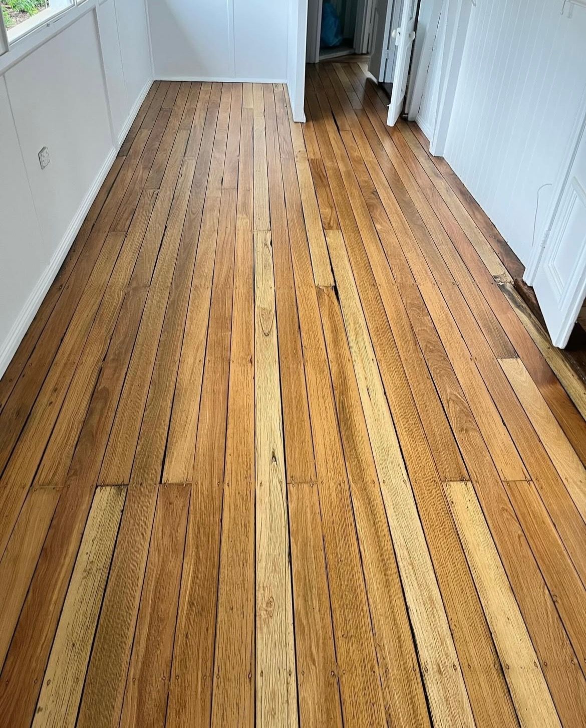 Wooden floorboards in a room. Light brown with some discolouration. White walls and doorway in the background. — Tweed Coast Cork & Timber Floors In Tweed Heads, NSW