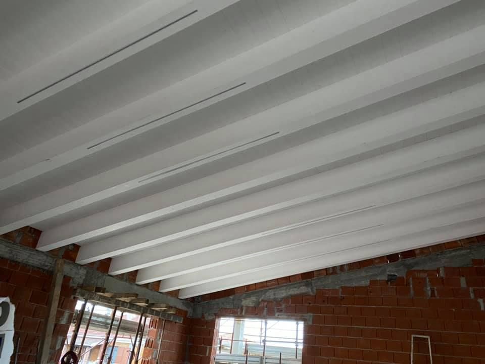 Travi del soffitto in cemento in un cantiere edile, sostenute da muri in mattoni e impalcature provvisorie.