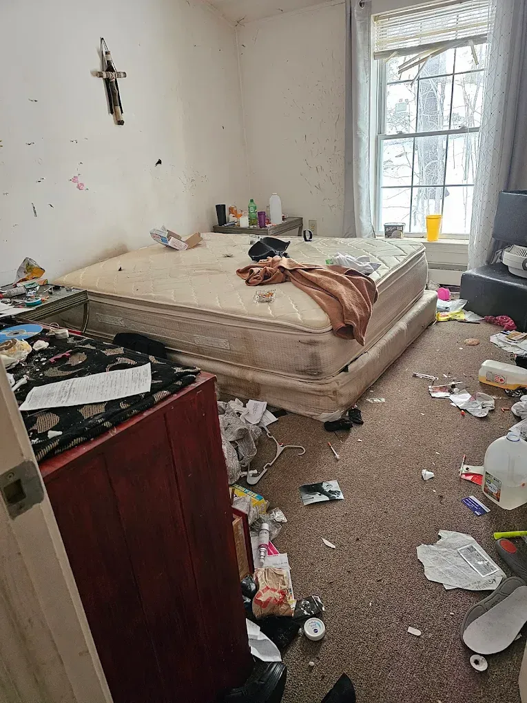 A bedroom with a bed and a lot of trash on the floor.