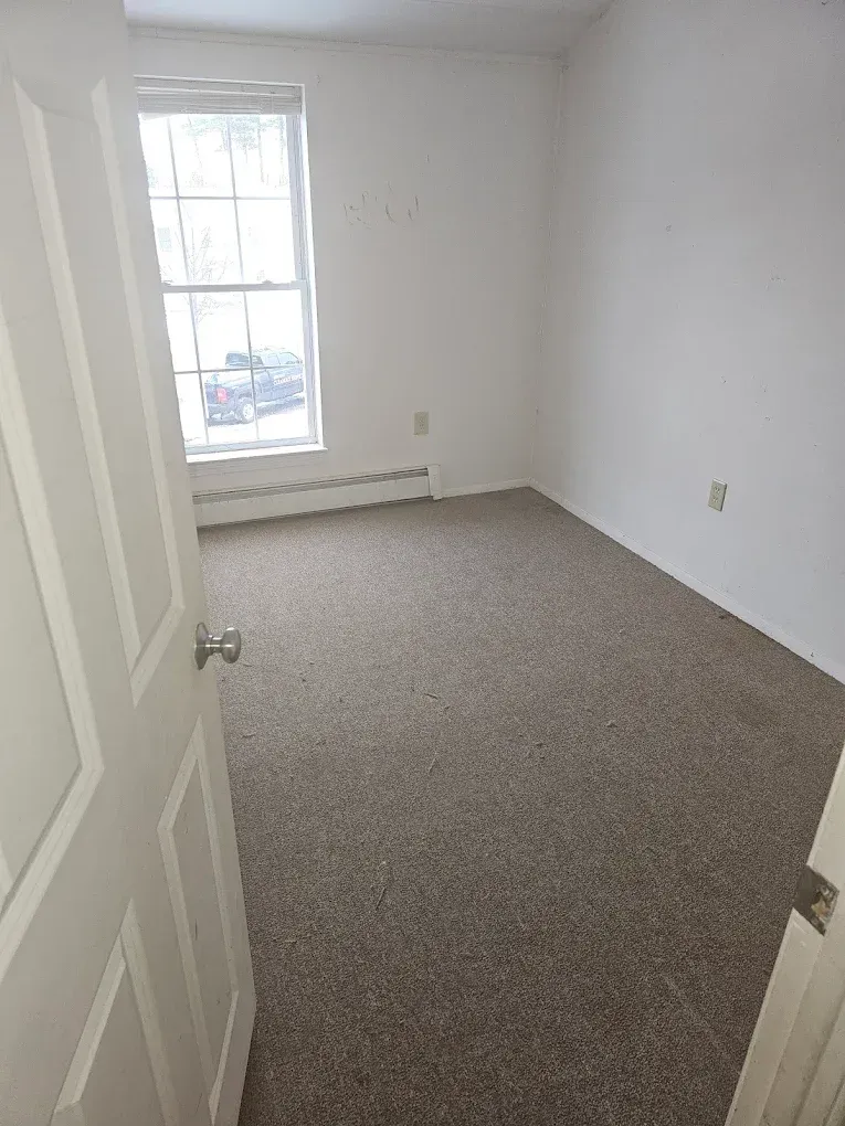 An empty bedroom with a carpeted floor and a window.