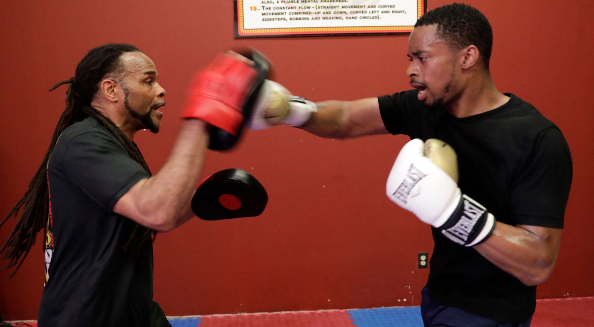 Two men wearing everlast boxing gloves are sparring in a gym