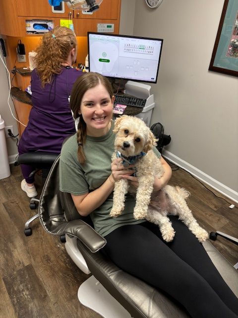 A woman is sitting in a dental chair holding Watson.