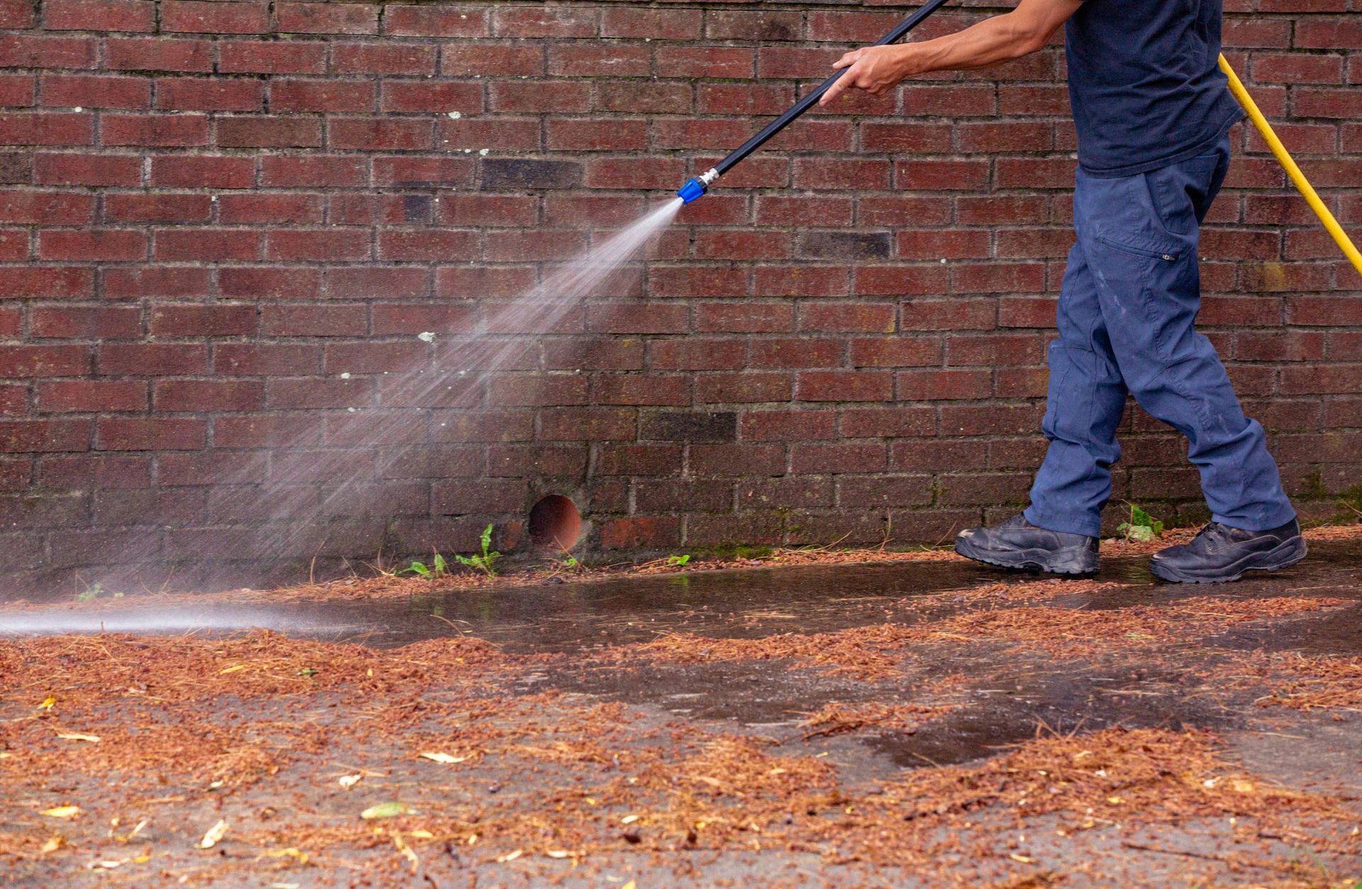 A man is using a high pressure washer to clean a brick wall.