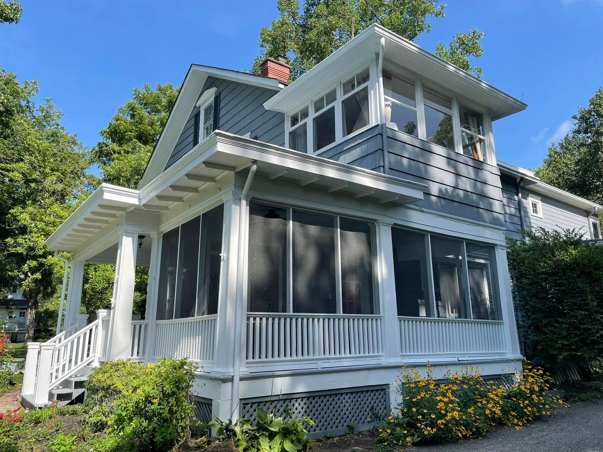 A white house with a screened in porch is surrounded by trees.