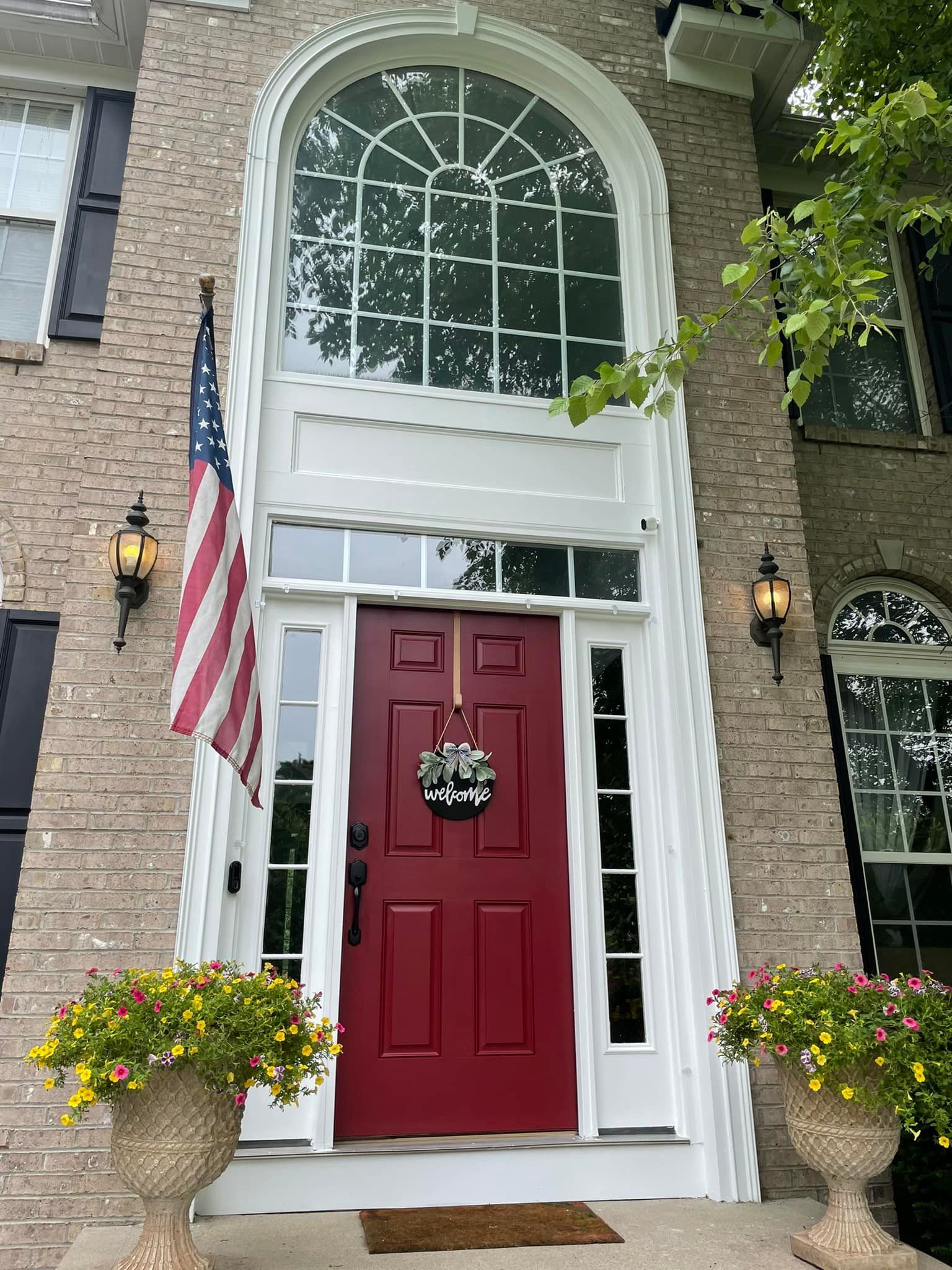 A red door with a wreath on it is on the front of a brick house.