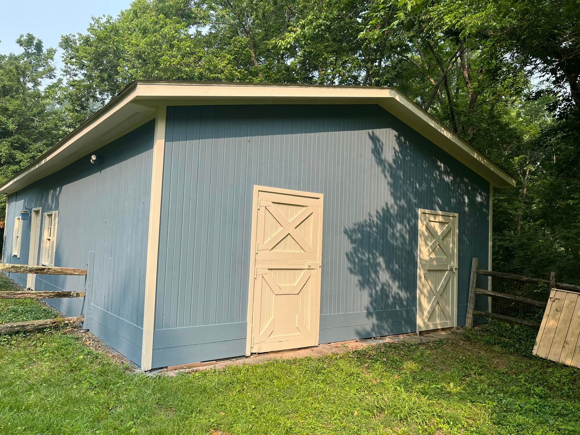 A blue barn with white doors is in the middle of a grassy field.