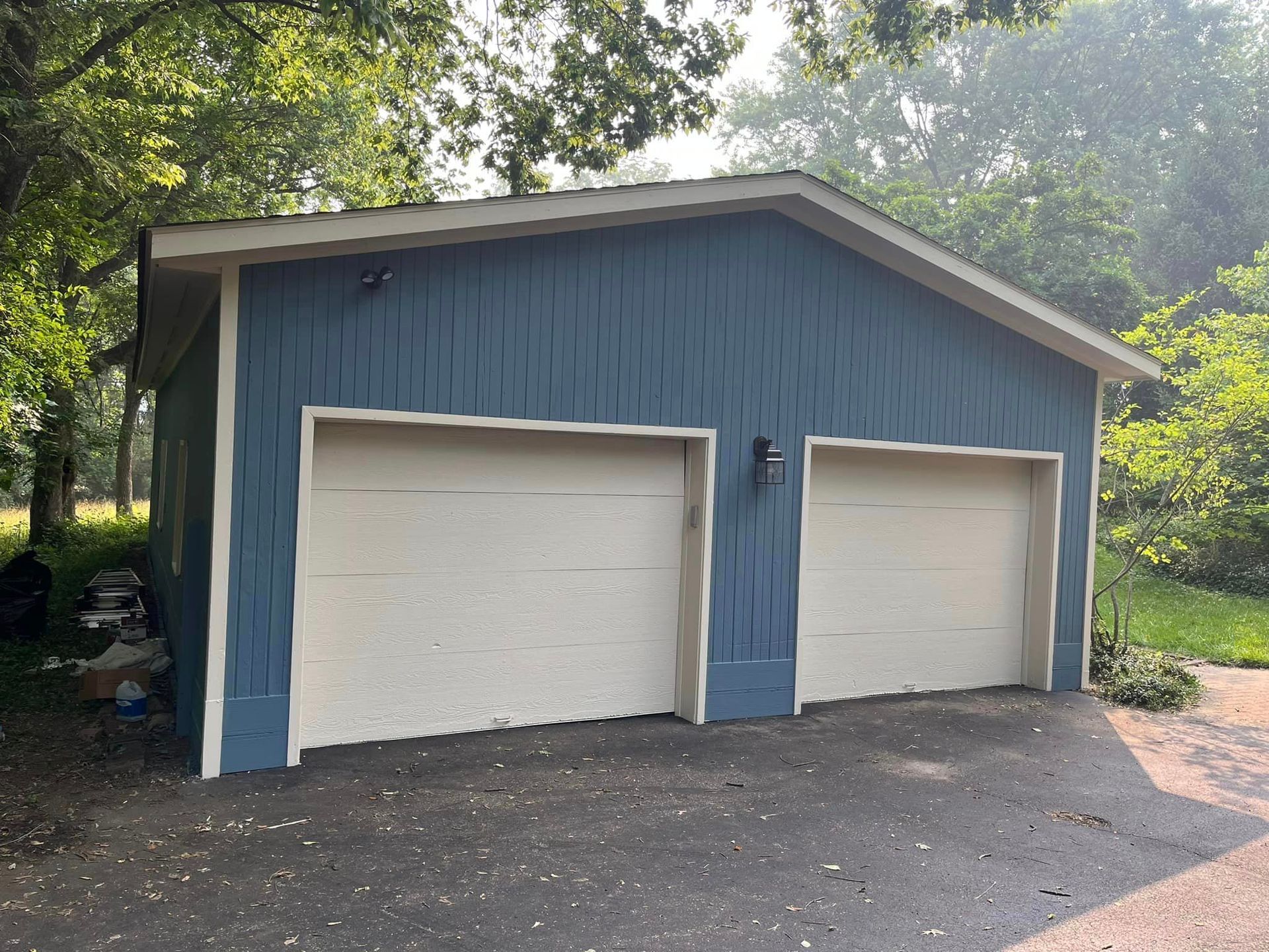 A blue garage with two white garage doors and a roof.