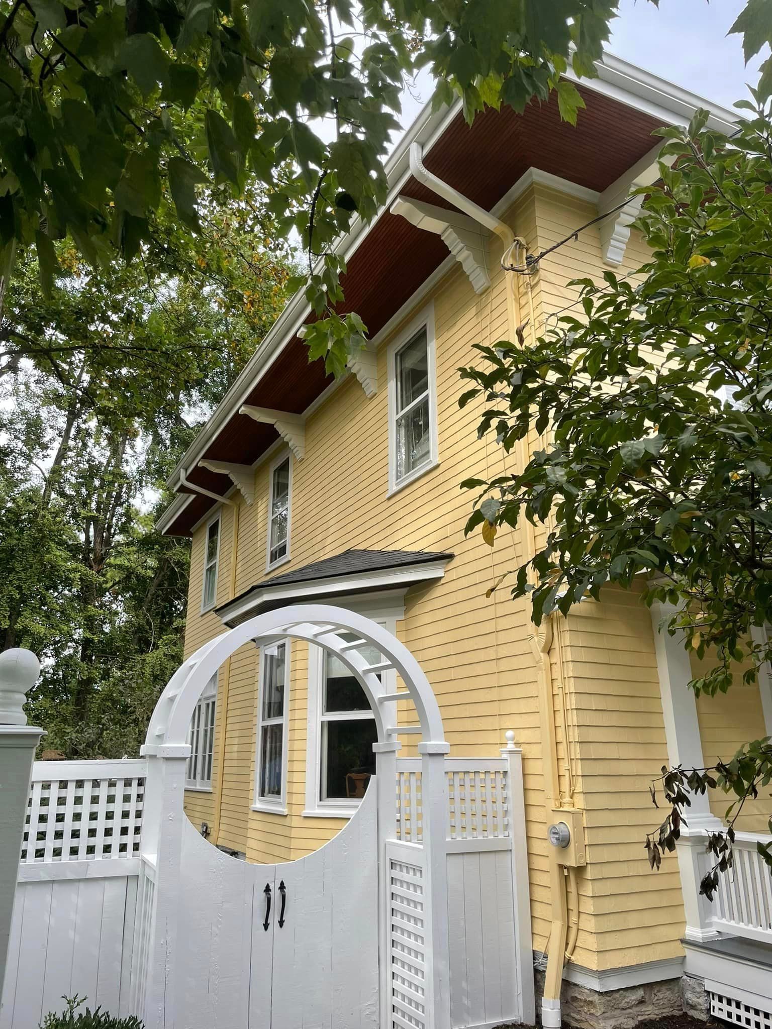 A yellow house with a white gate in front of it surrounded by trees.