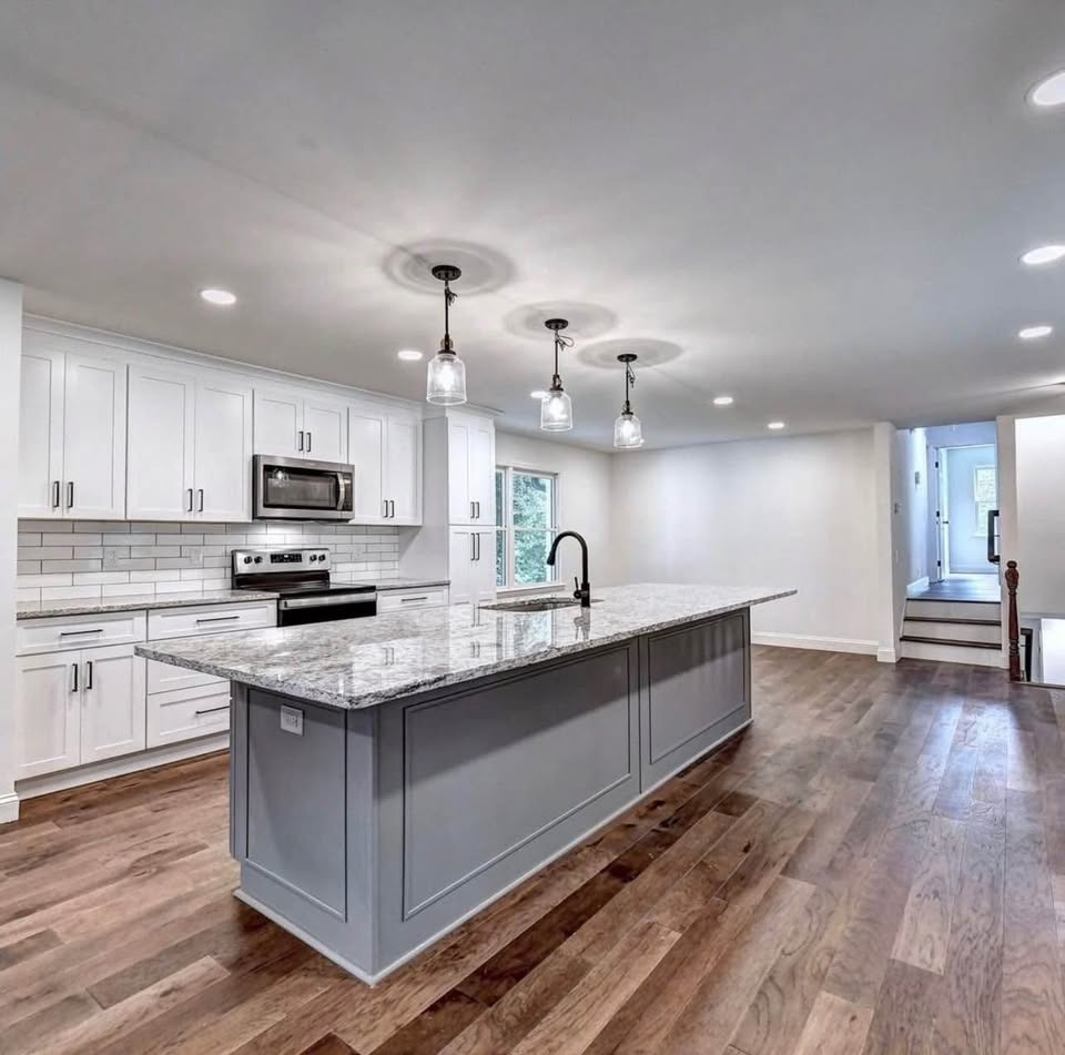 Modern kitchen with white cabinets, gray island, granite countertops, and hardwood floors.