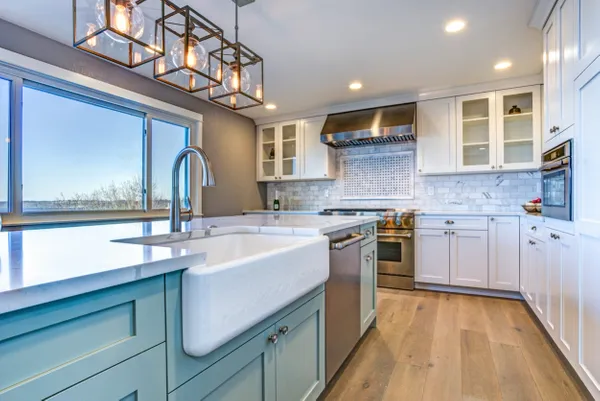 Modern kitchen with blue island, white cabinets, and light wood floors. Large window and pendant lights.