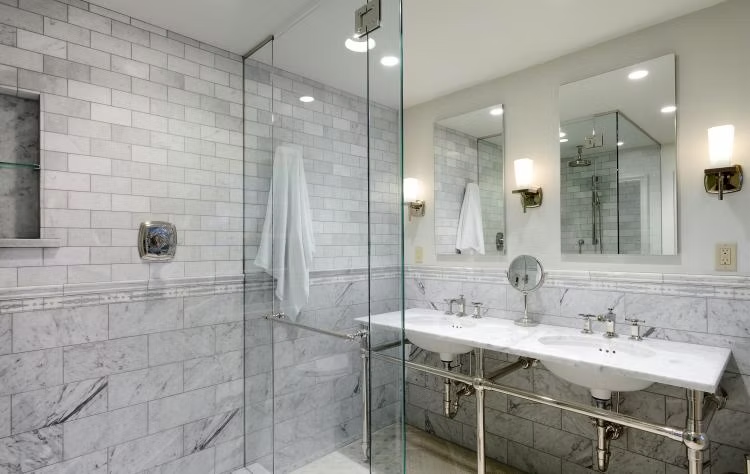 Elegant marble bathroom with glass shower, double vanity, and large mirrors.