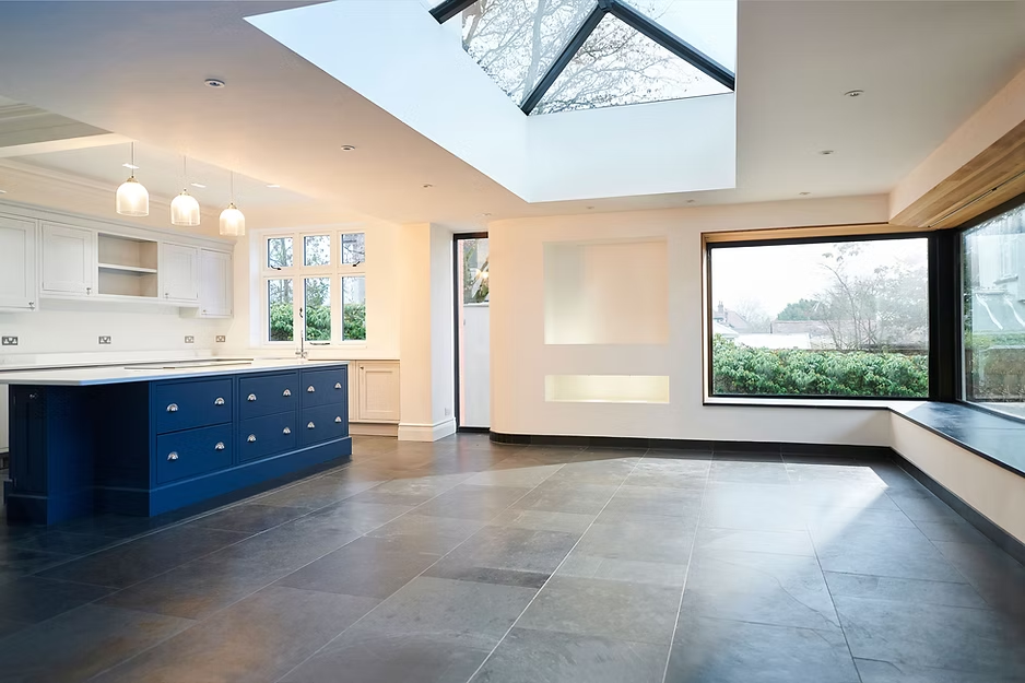 Spacious modern kitchen with a blue island, skylight, and large windows with a view of greenery.