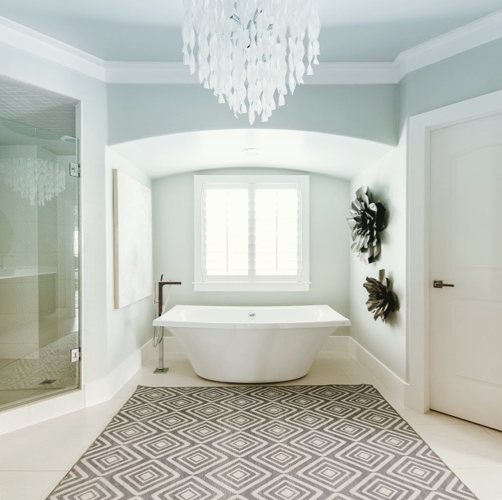 Elegant white bathroom with freestanding tub, geometric rug, and chandelier.