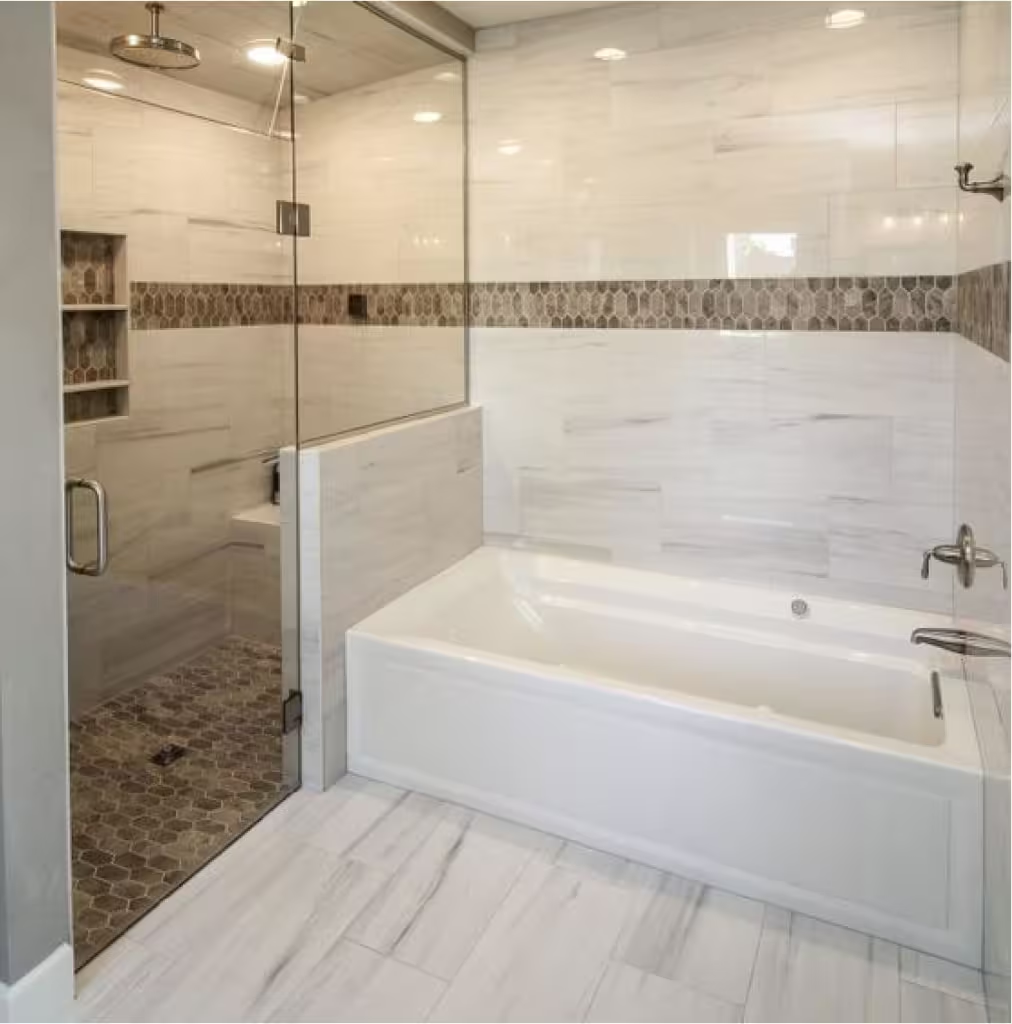 Modern bathroom with glass shower, white bathtub, and marble tile accents.