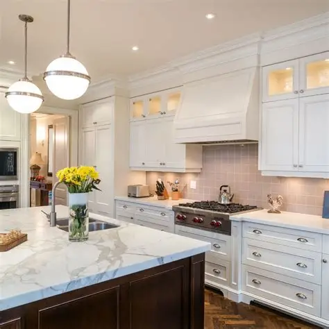 Elegant white kitchen with marble island, dark brown base, and spherical pendant lights.