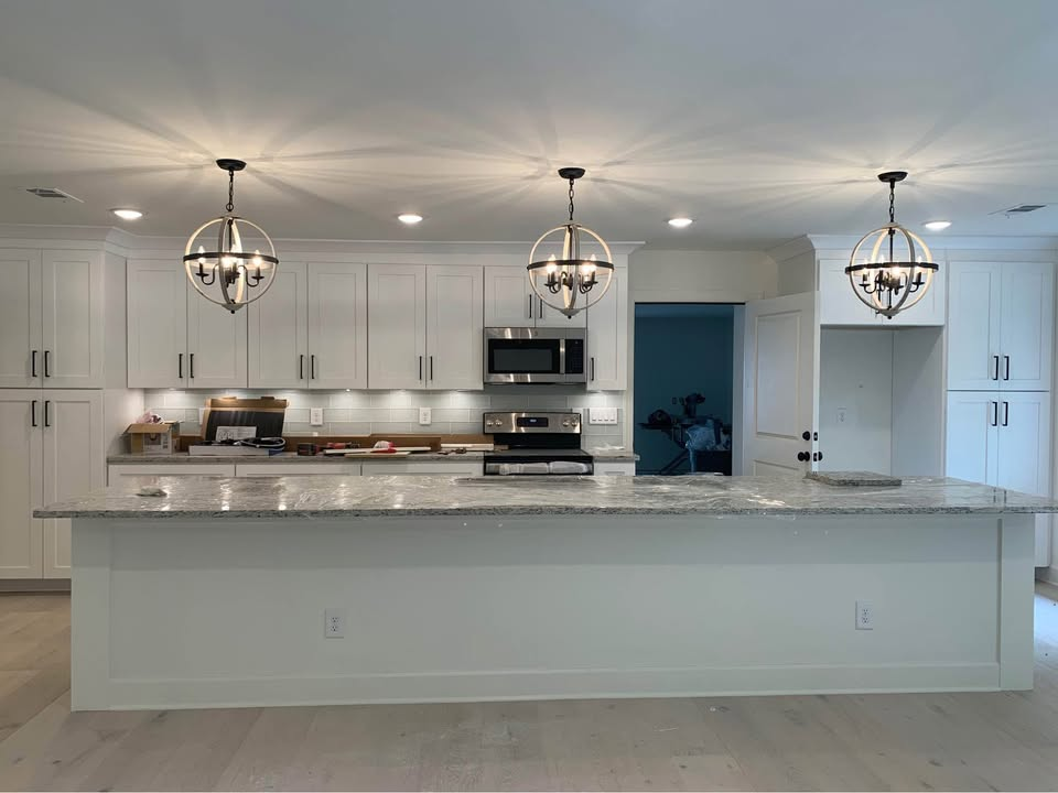 White kitchen with island, cabinets, and pendant lights. Stainless steel appliances.