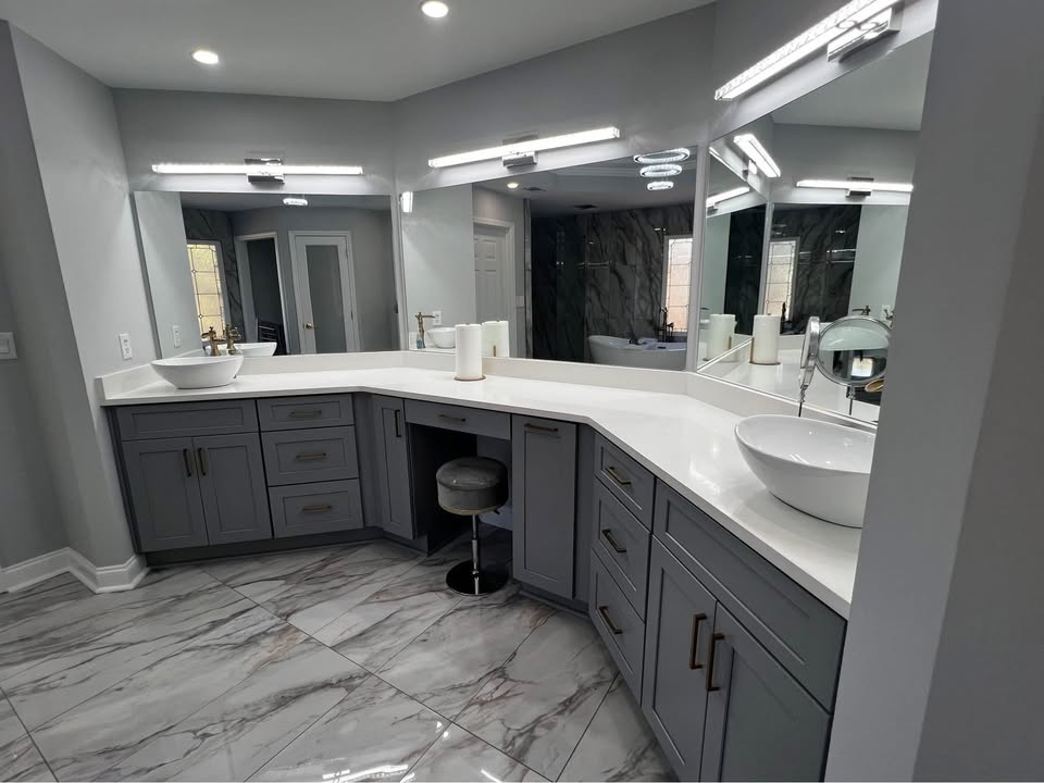 Gray bathroom with large mirrors, two sinks, vanity, and marble flooring.