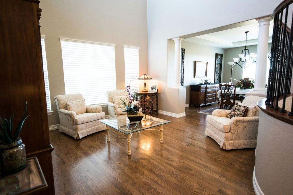 Living room with wood floor, three armchairs, glass coffee table, and an open view into a dining area.