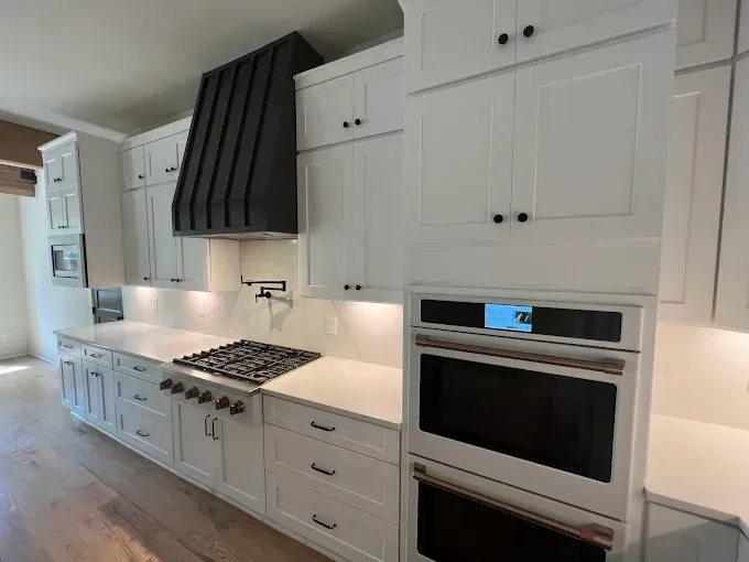White kitchen with a black hood, stainless steel stove and ovens.