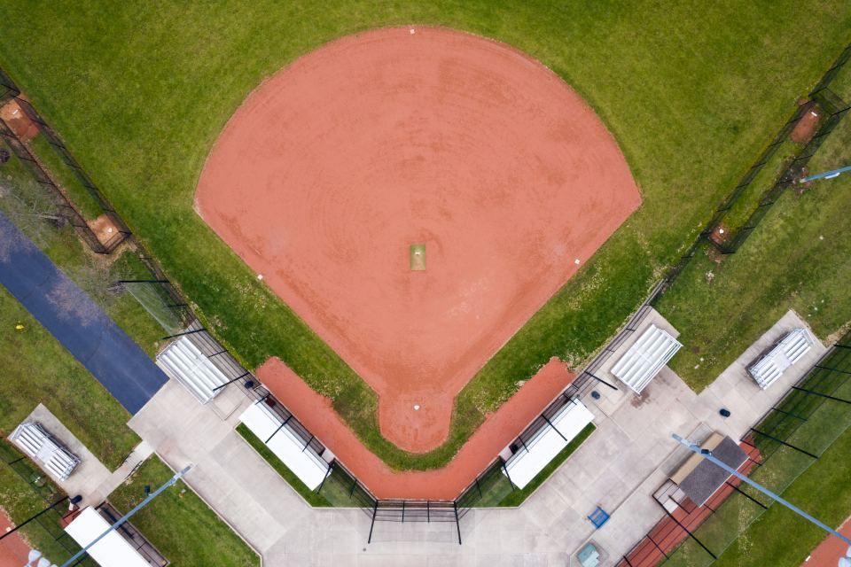 Aerial view of a baseball field with orange infield, green outfield, and surrounding bleachers.